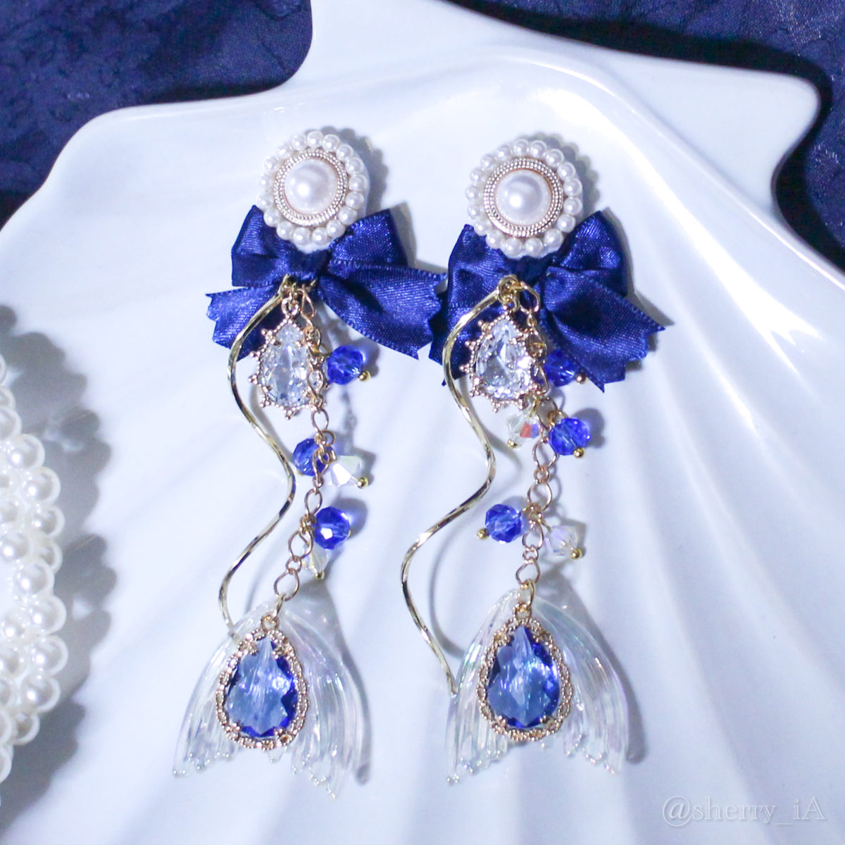 アミュリボン 海の雫とロイヤルブルーマーメイド 耳飾り 雫型のビジュー2つとブルーとクリアのガラスカットビーズをたくさん使って作った人魚姫モチーフのハンドメイドアクセサリー 貝殻の上で撮影されたピアス/イヤリング ネイビー